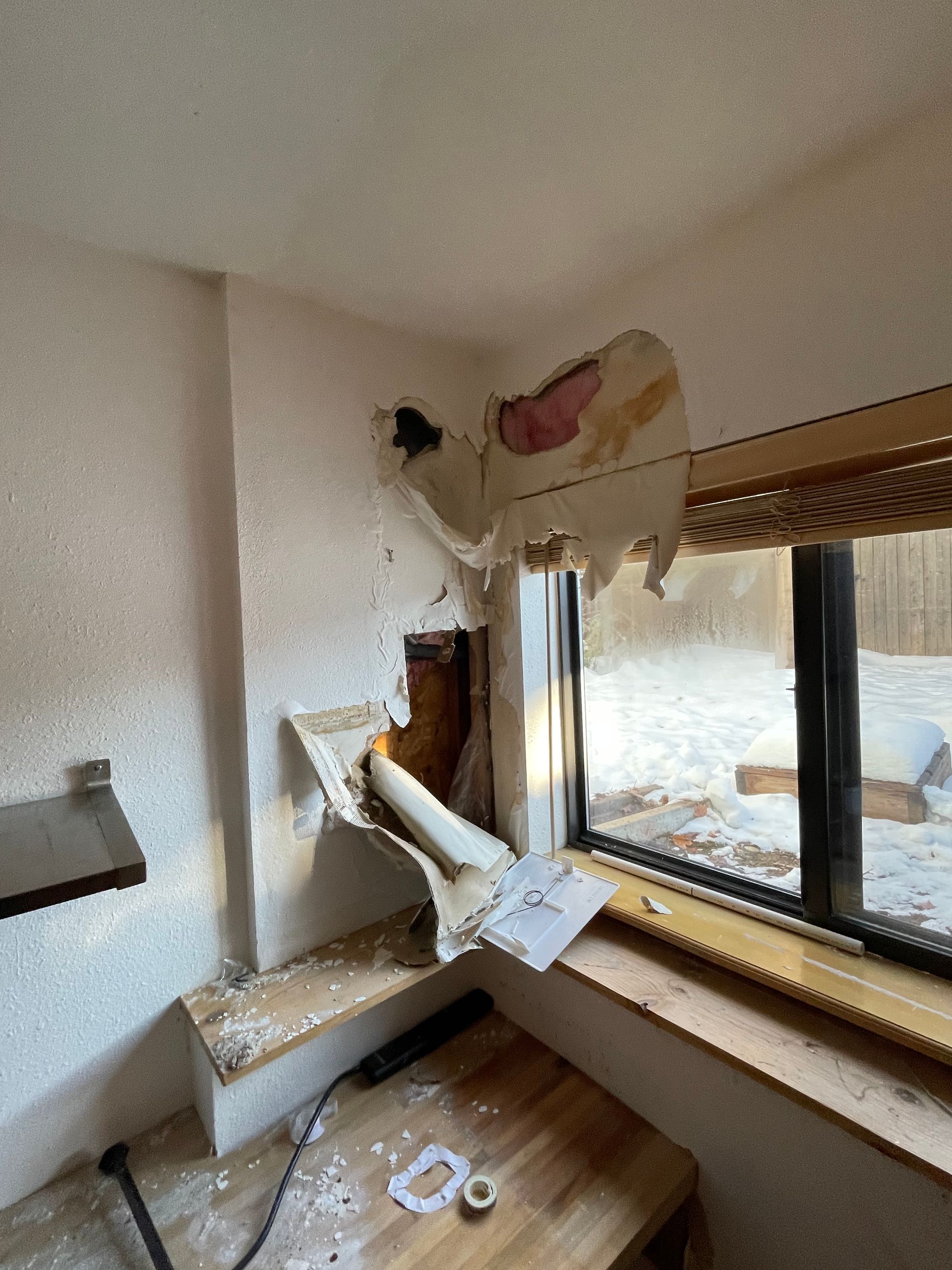 Damaged bedroom wall and broken window with debris on floor and window ledge