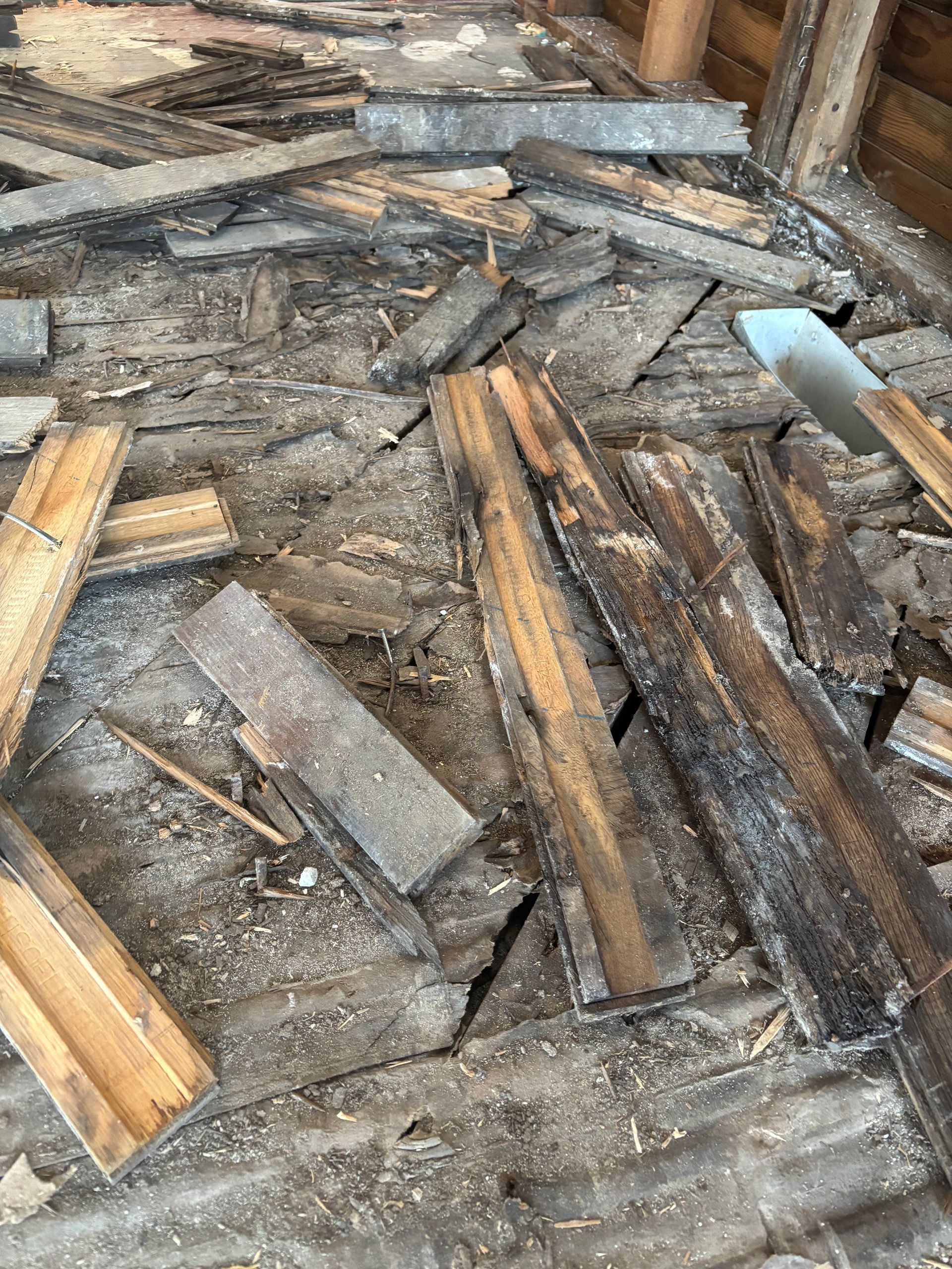 Scattered weathered wood planks and broken boards on a rough floor, with a blue-handled tool at right