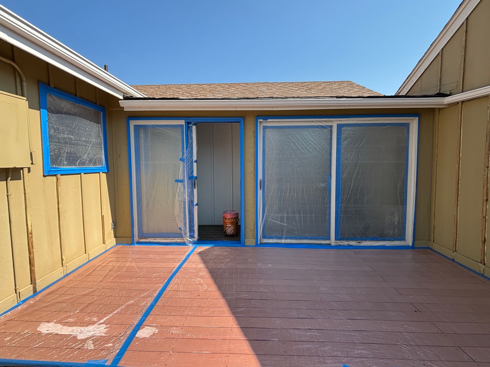 Back patio with tan walls, blue trim, and sliding glass doors under bright sunlight.