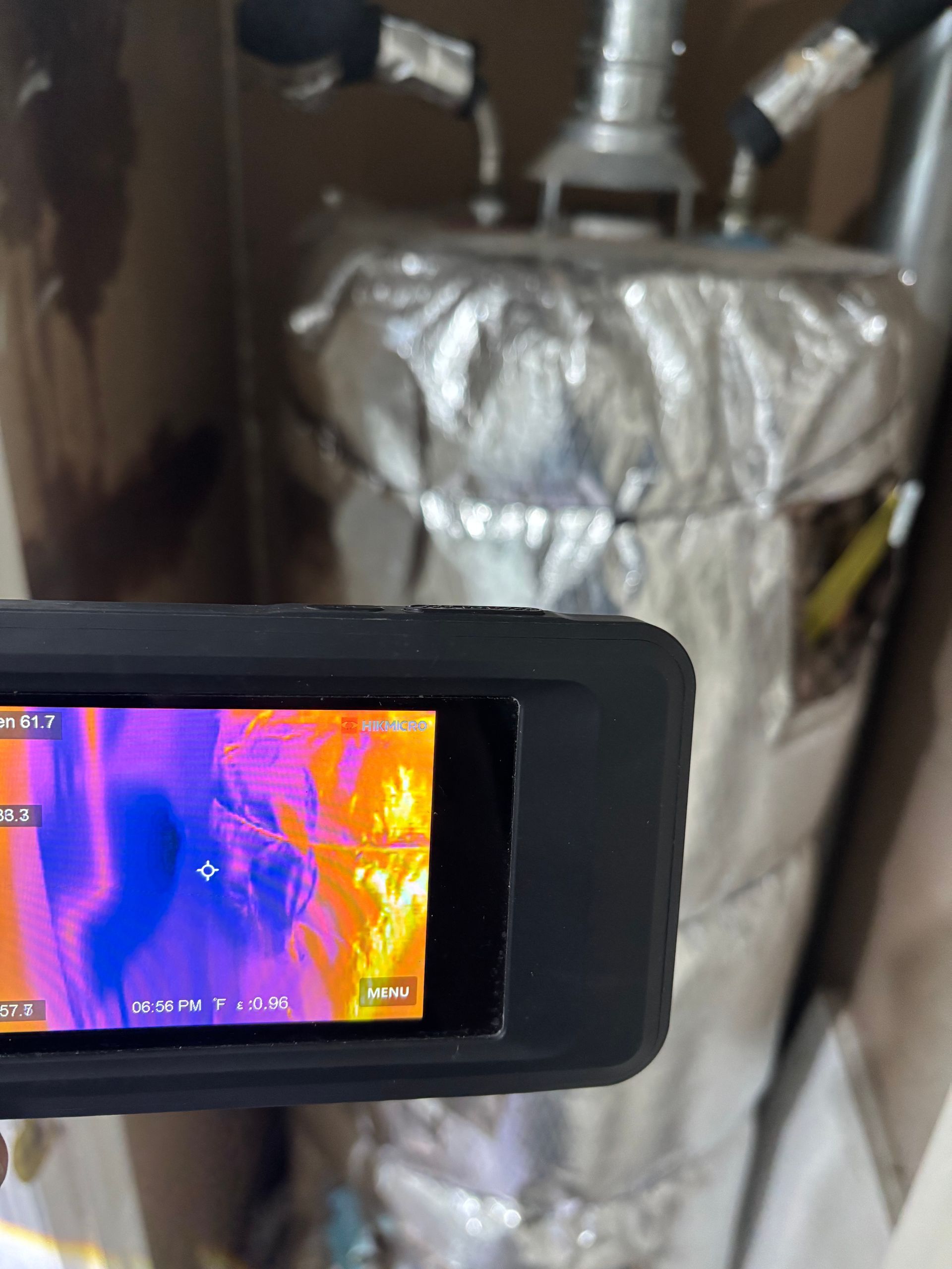 Thermal camera screen showing hot pipes and a wrapped metal tank in a utility room