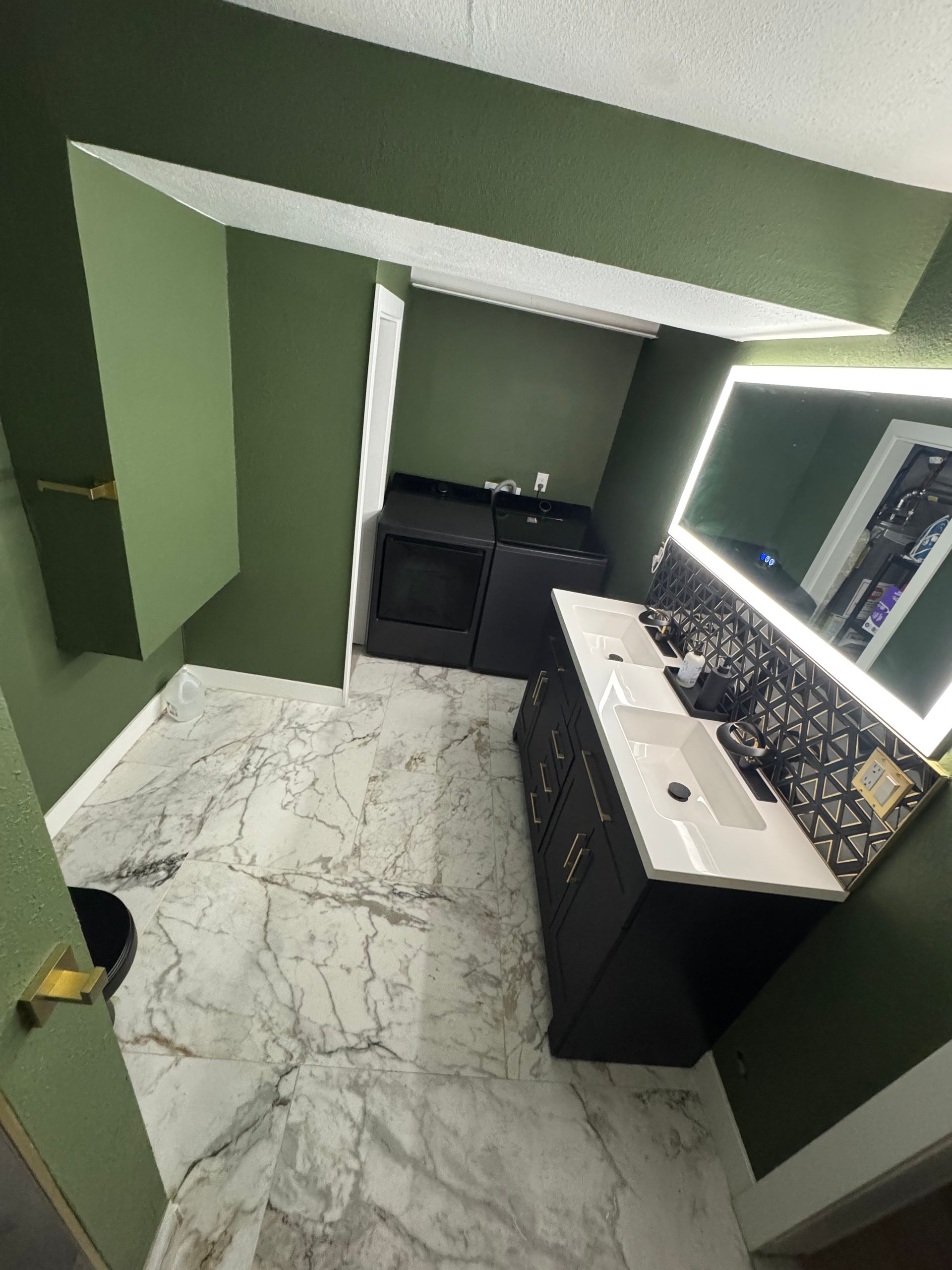 Compact green bathroom with white marble floor, sink vanity, mirror, and a partially open door.