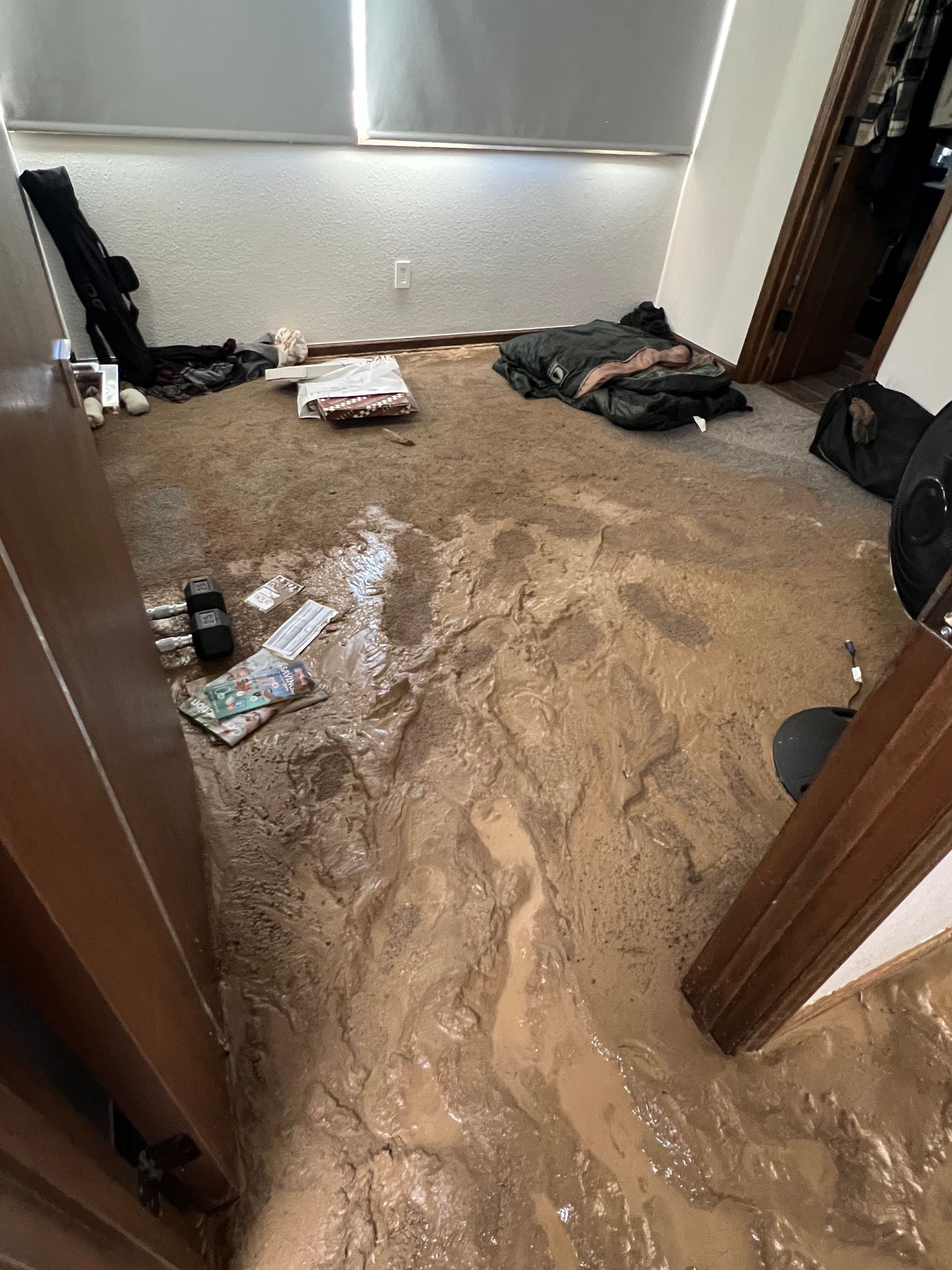 Indoor room flooded with muddy brown water, covering the floor and scattered belongings.
