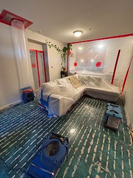 Living room covered for painting, with furniture draped in plastic and supplies on the floor