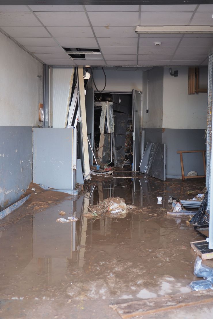 Flood-damaged hallway with muddy standing water, damaged ceiling tiles, and debris scattered along the corridor.