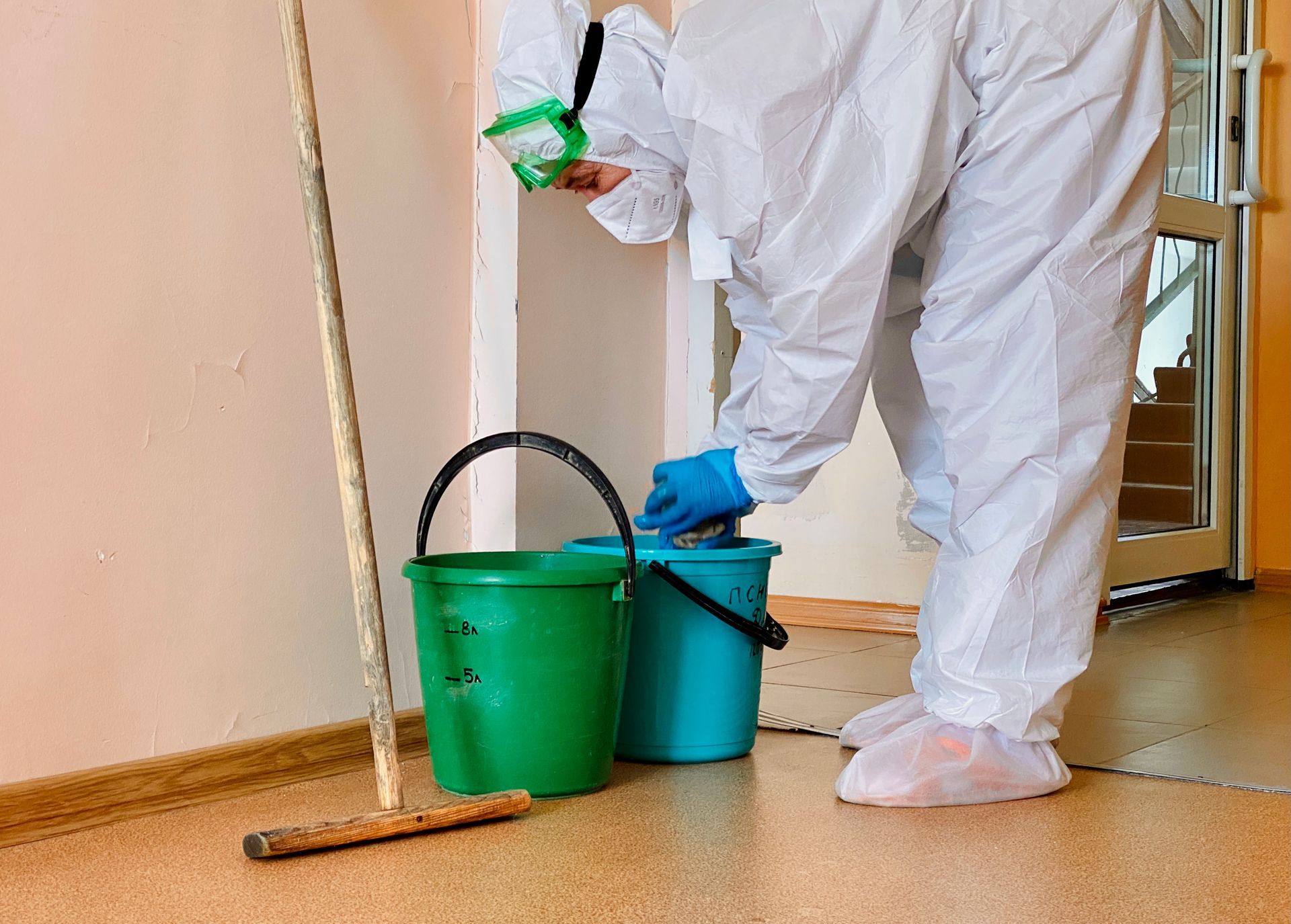 Person in white coveralls cleaning a floor with a green bucket and blue gloves