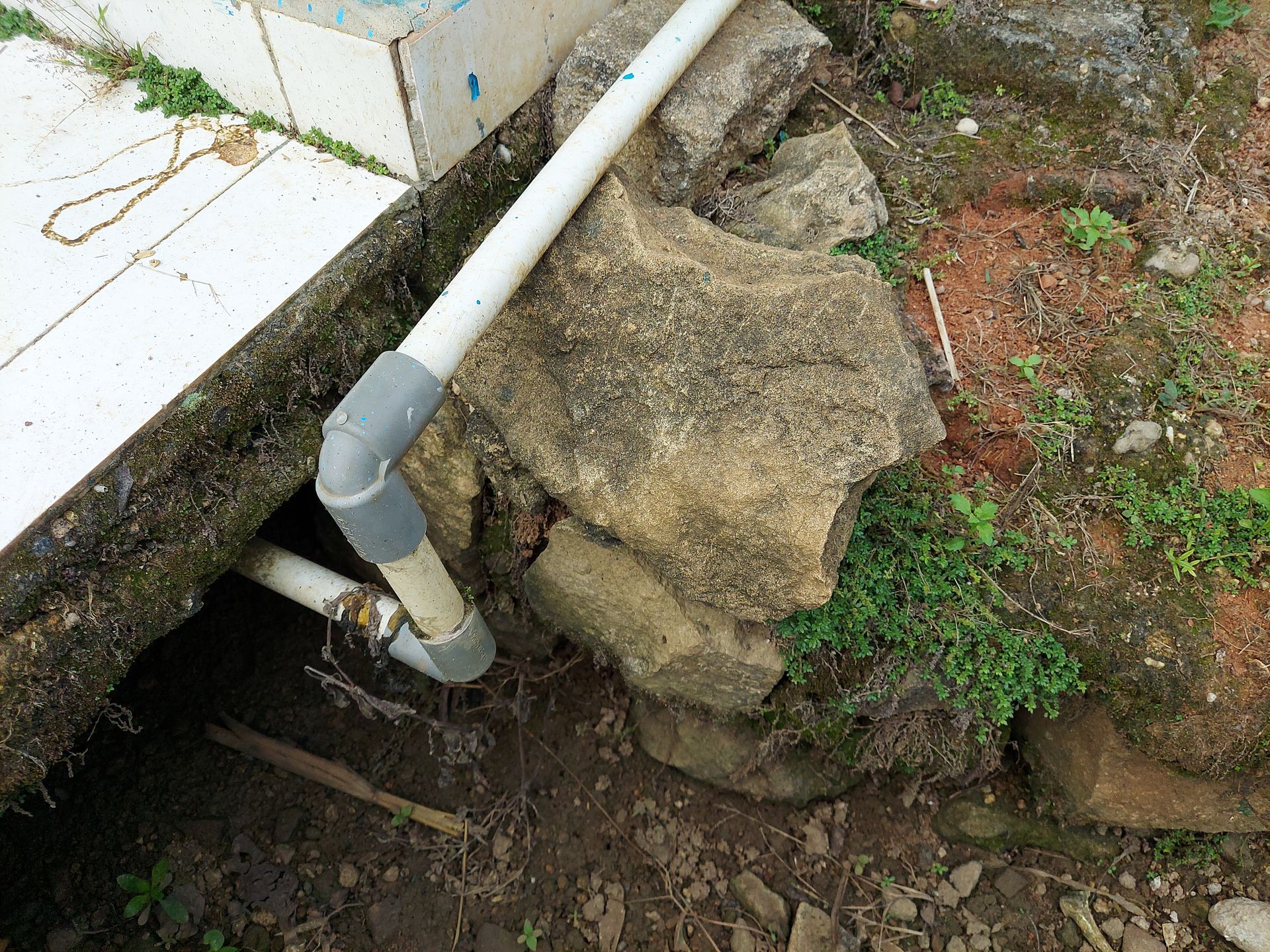 Concrete pipe beside a rocky drainage channel with dirt and green groundcover