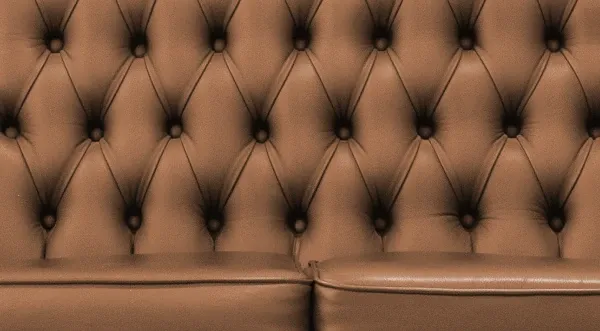 Nahaufnahme der Rückenlehne eines braunen, gesteppten Ledersofas mit rautenförmigem Knopfmuster.
