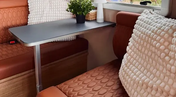 Eine gemütliche Sitzecke im Wohnmobil mit rostfarbenen, strukturierten Kissen, einem kleinen Tisch