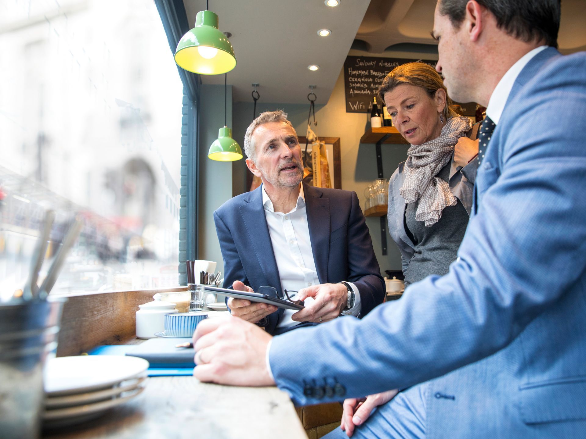 Three people in a cafe discussing a tablet at a table.