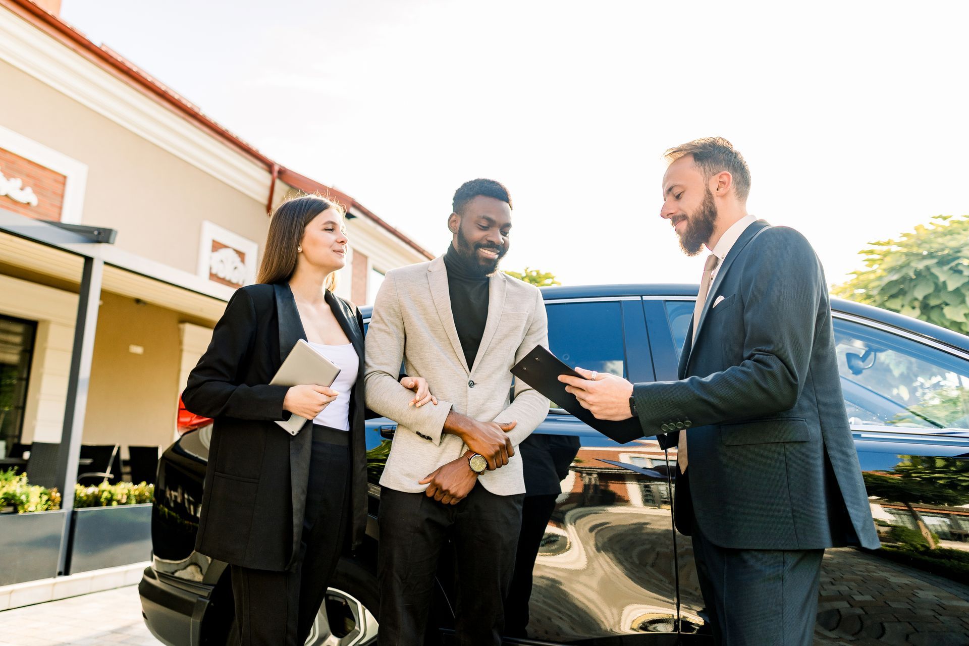Three businesspeople discussing paperwork beside a black car outside a building