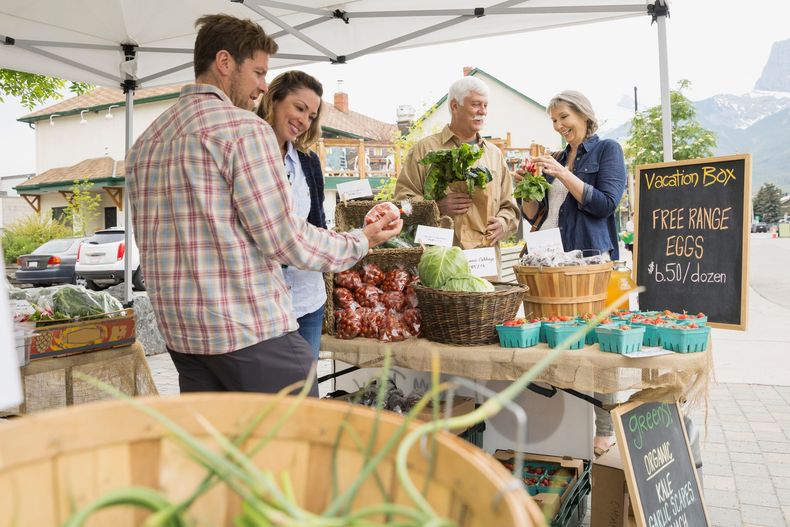 Farmers market stall with fresh produce, baskets, and a chalkboard menu under a white canopy.