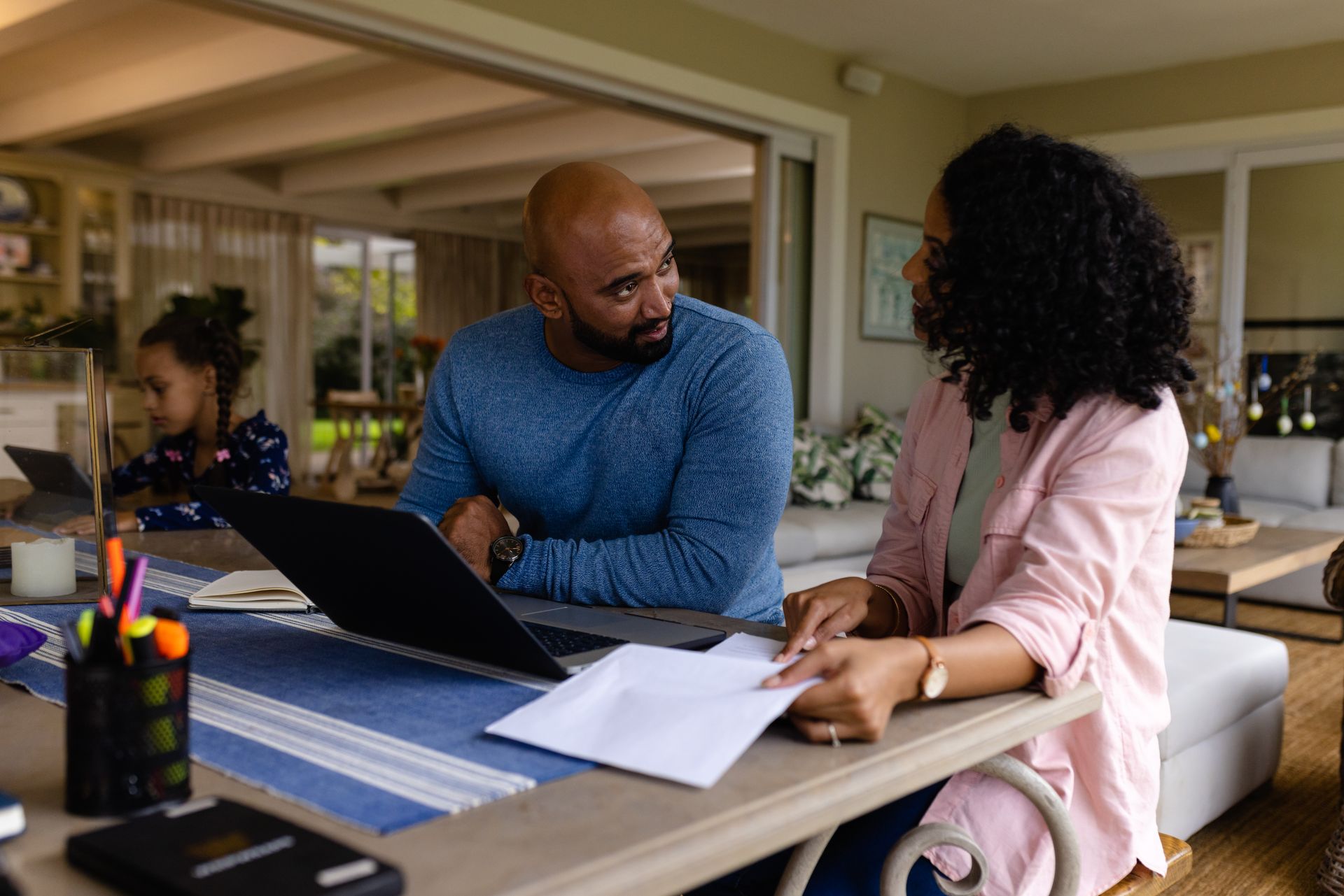 Two people talking at a patio table with a laptop and papers on a covered porch