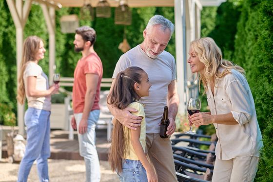 People chatting and hugging outdoors at a sunny gathering, with benches and trees in the background
