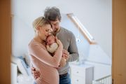 Couple holding a newborn baby in a bright nursery, standing close together and smiling.