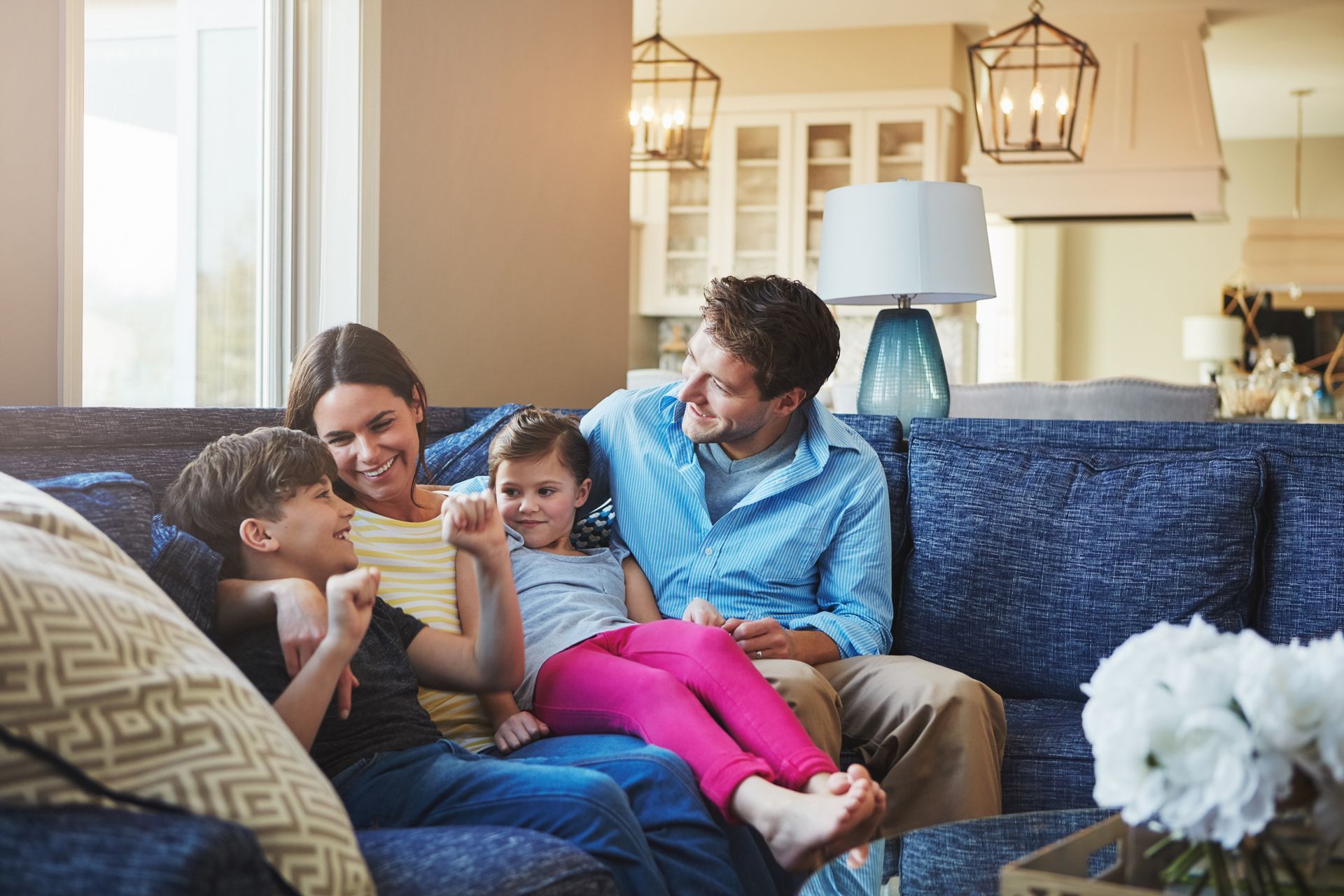 Family relaxing on a couch in a bright living room, smiling and looking at a phone together.
