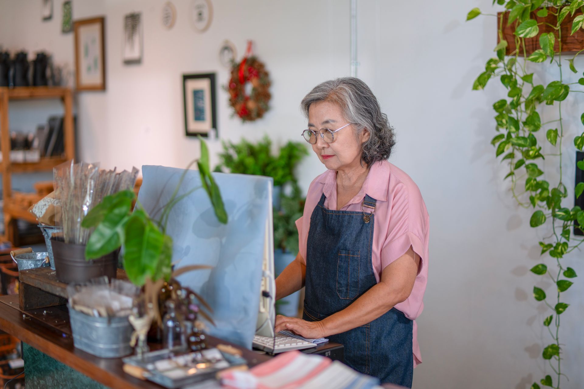Woman working on a laptop in a cozy home office with plants and wall art.