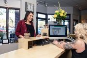 Customer and cashier at a salon checkout desk, with a computer monitor and flowers in the background.