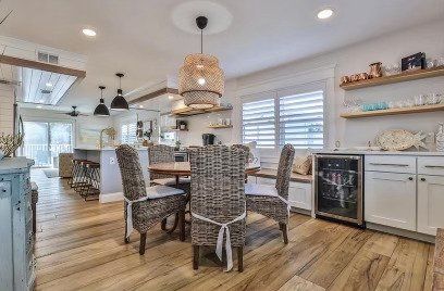 Dining area with wicker chairs, a wooden table, and a woven pendant light, opening into a kitchen with light wood floors.