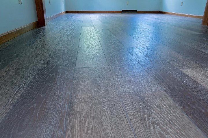 A low-angle view of wide-plank, grey-toned wood flooring extending toward a pale blue wall with brown trim.