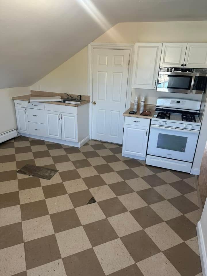 A kitchen with white cabinets, a stove, a microwave, and a checkered brown-and-white floor under a sloped ceiling.