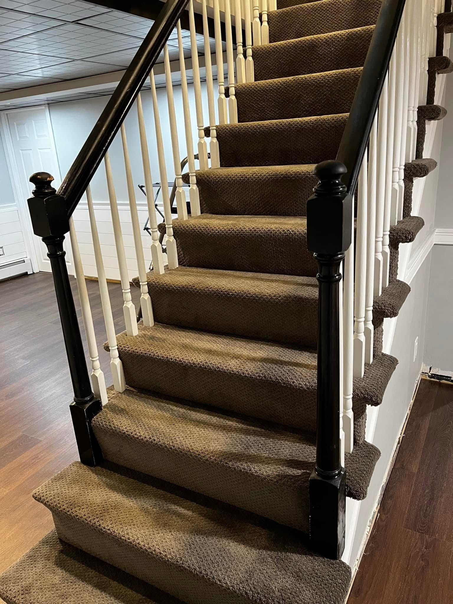 Stairs with brown carpet, white balusters, and black wooden newel posts, leading upward in an indoor residential setting.