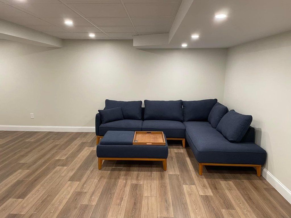 A navy blue sectional sofa and matching ottoman with a wooden tray sit in an empty room with light walls and wood floors.