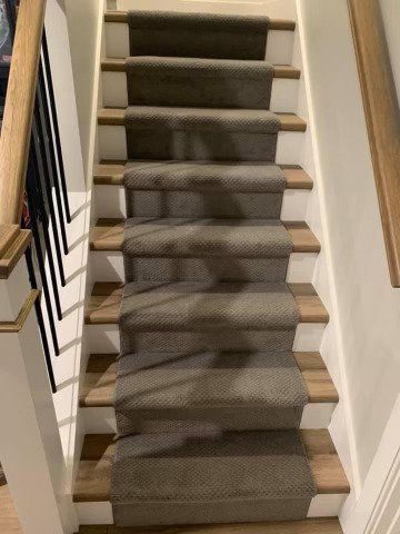 A staircase with dark gray carpeted treads on wooden steps, white risers, and a wooden handrail with black spindles.