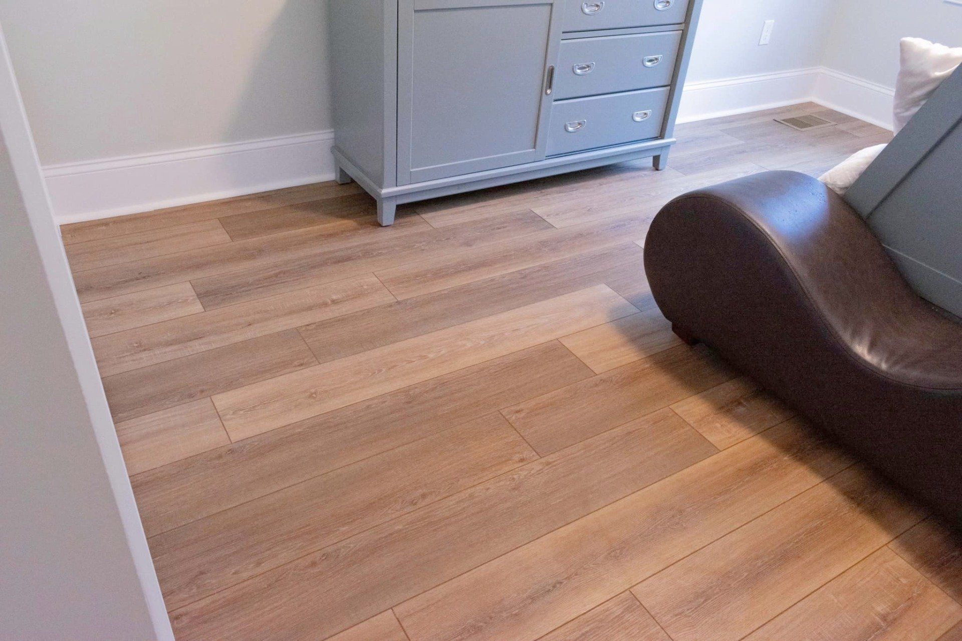 Light oak wood-look plank flooring in a room with a gray dresser and a dark brown curved lounge chair.