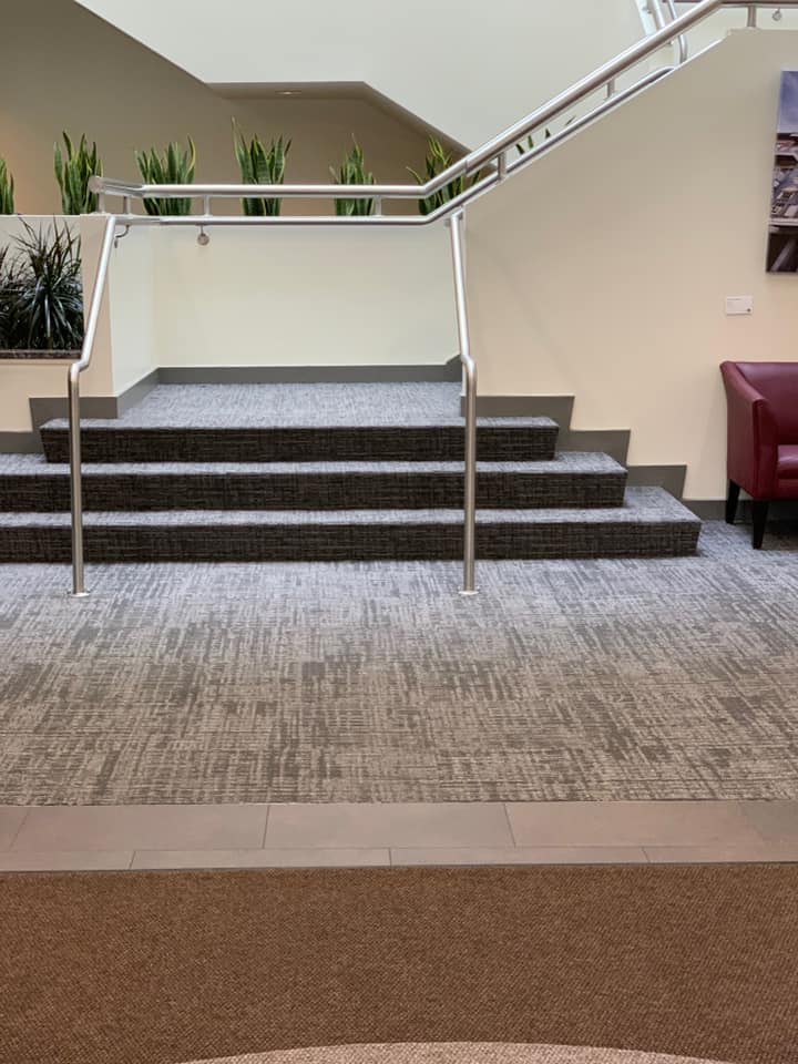 A staircase with three carpeted steps and silver handrails in a modern, neutral-toned interior space.