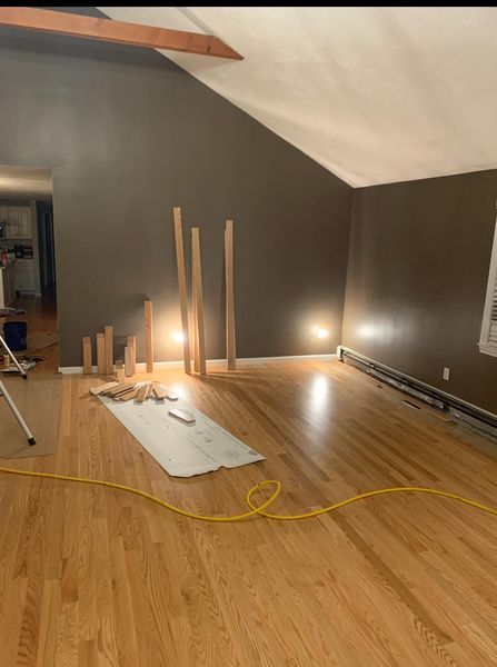 A room with dark brown walls and hardwood floors, featuring several wooden boards leaning against the wall during renovation.