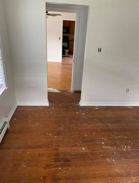 A doorway opens to an adjacent room, both featuring light-colored walls and wood flooring with minor surface debris.