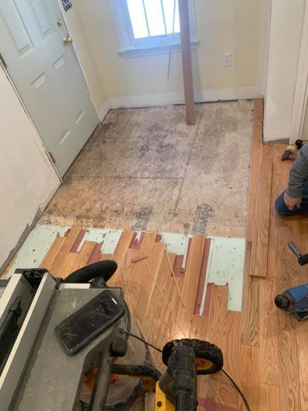 Hardwood floor installation in progress, showing exposed subfloor near a doorway and a person working on the side.