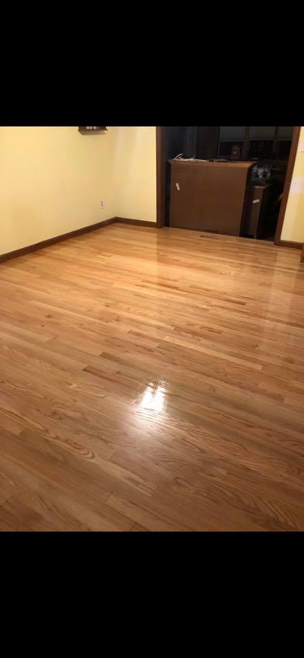 A freshly polished, light-brown hardwood floor in an empty room with light-yellow walls and a dark doorway.