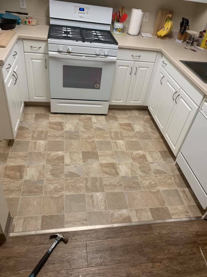 Kitchen with white cabinets, a gas stove, and tan tile flooring transitioning to wood flooring, with a hammer on the floor.