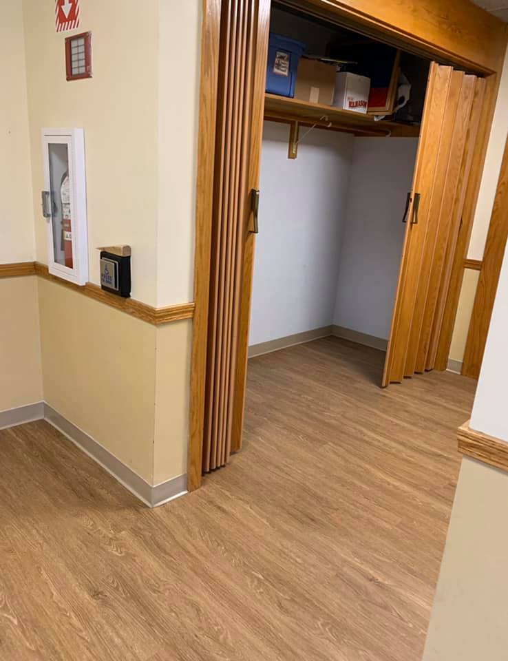 A hallway with light wood-look flooring, a wall-mounted fire extinguisher cabinet, and an open accordion-style wood closet.