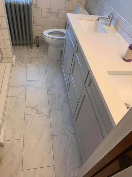A modern bathroom featuring a white vanity with two sinks, marble-patterned tile flooring, a toilet, and a radiator.