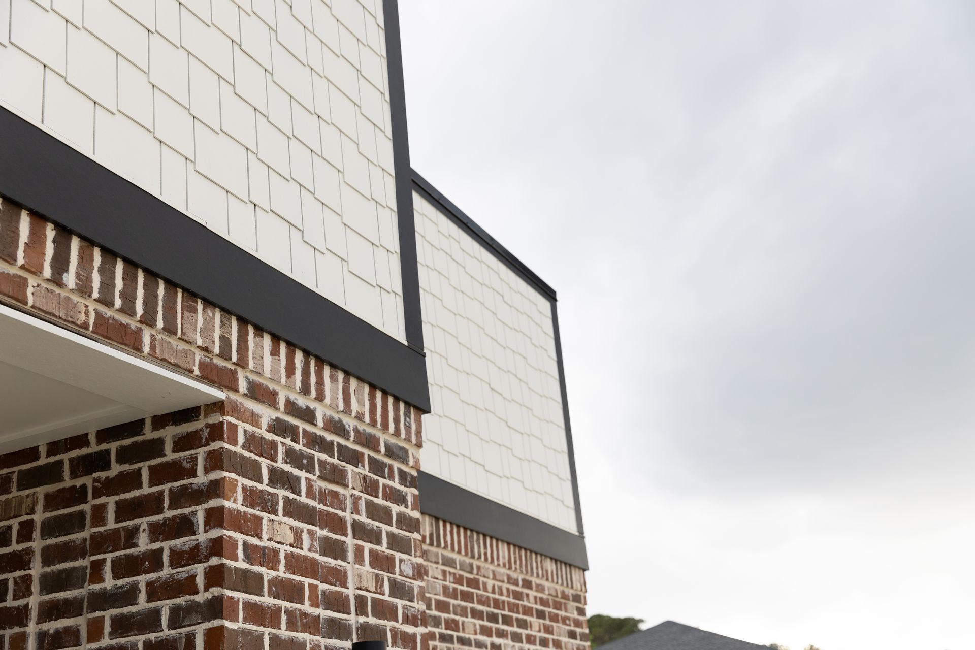 Brick building exterior with white paneling and dark trim against a cloudy sky.
