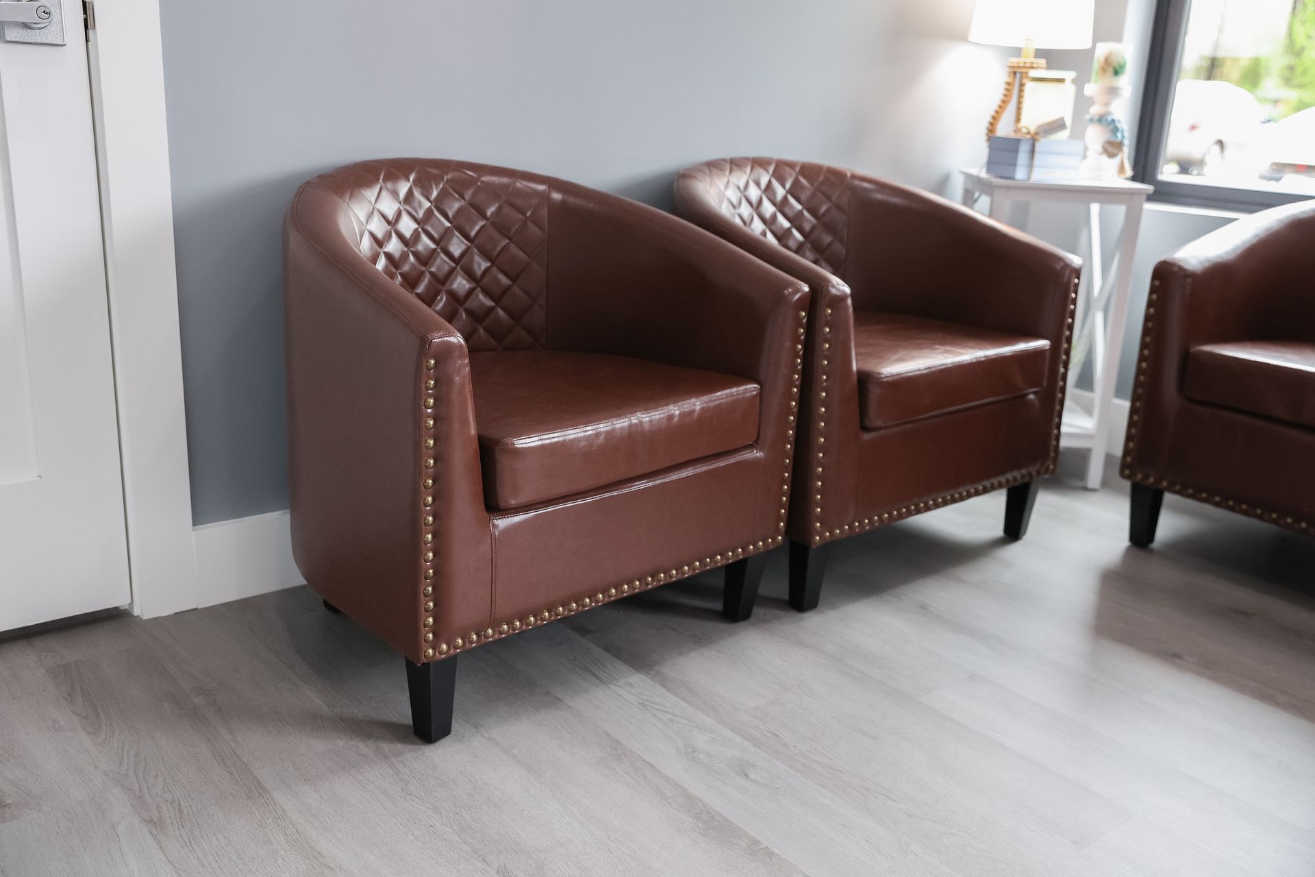 Three brown leather barrel chairs in a waiting area with gray walls and a white door.