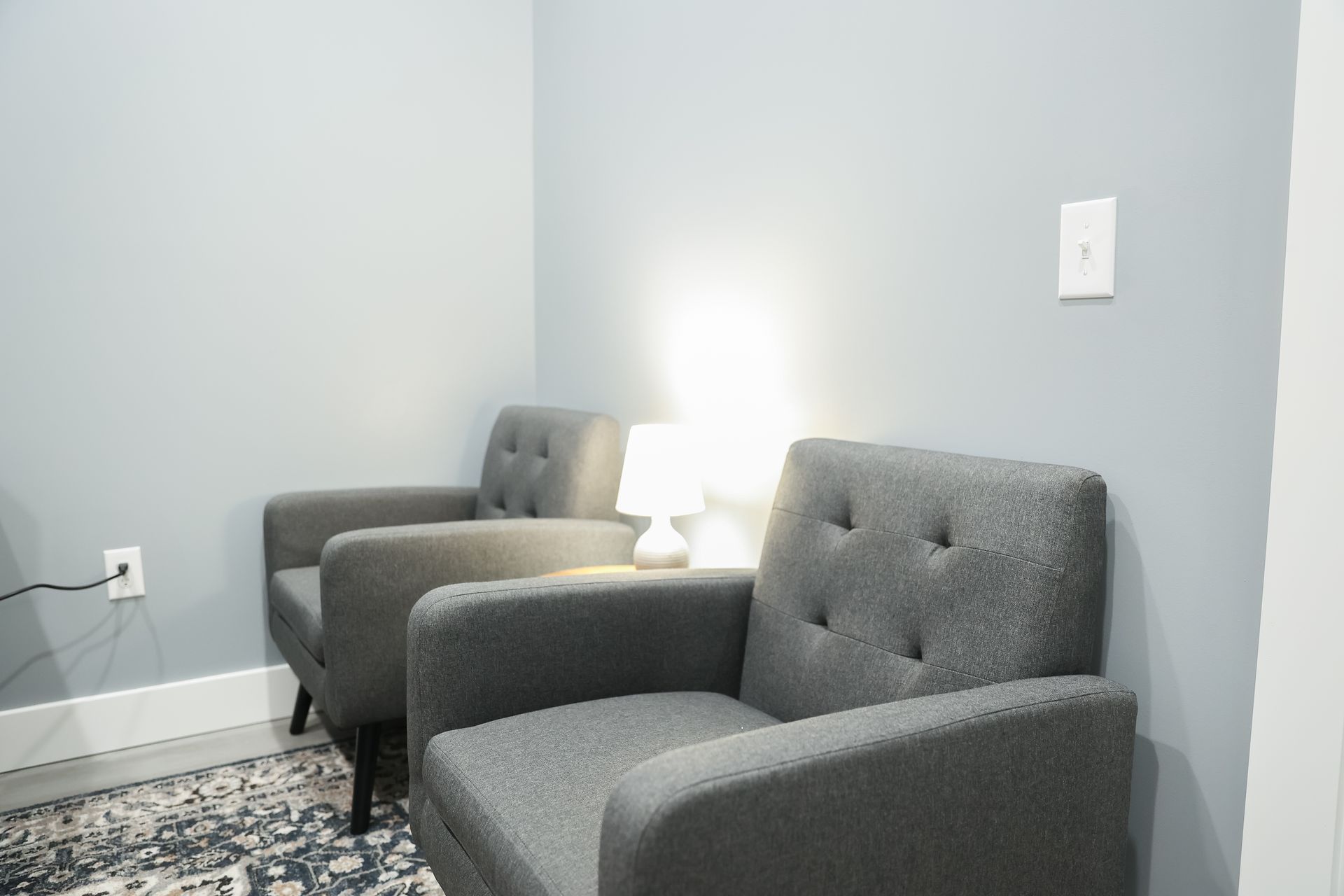 Two gray armchairs with a lamp sit against a gray wall in a corner.