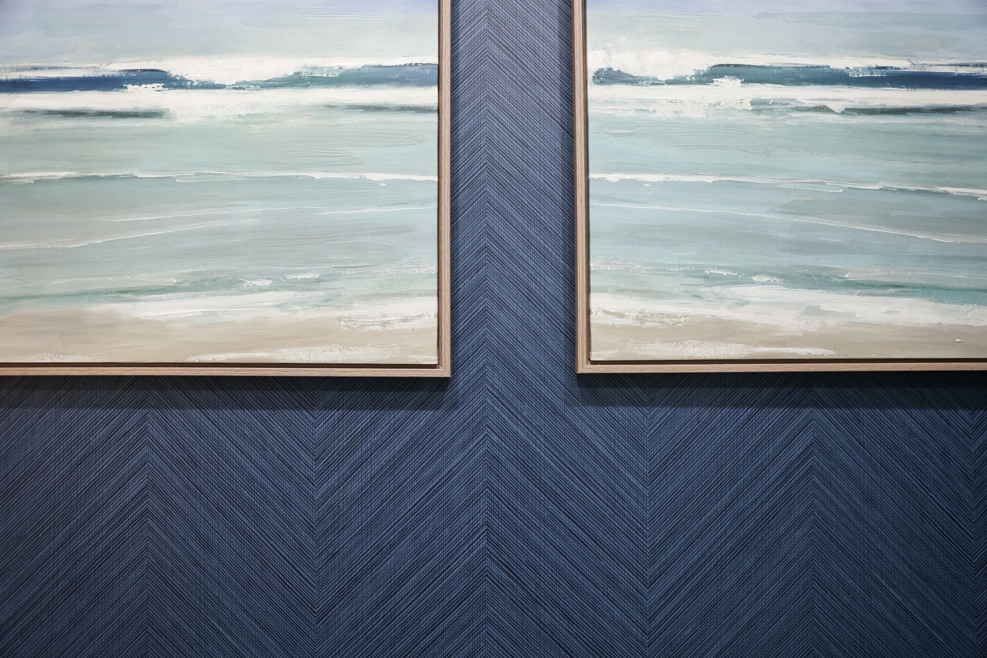 Two framed beach paintings hang on a dark blue, textured, chevron patterned wall.