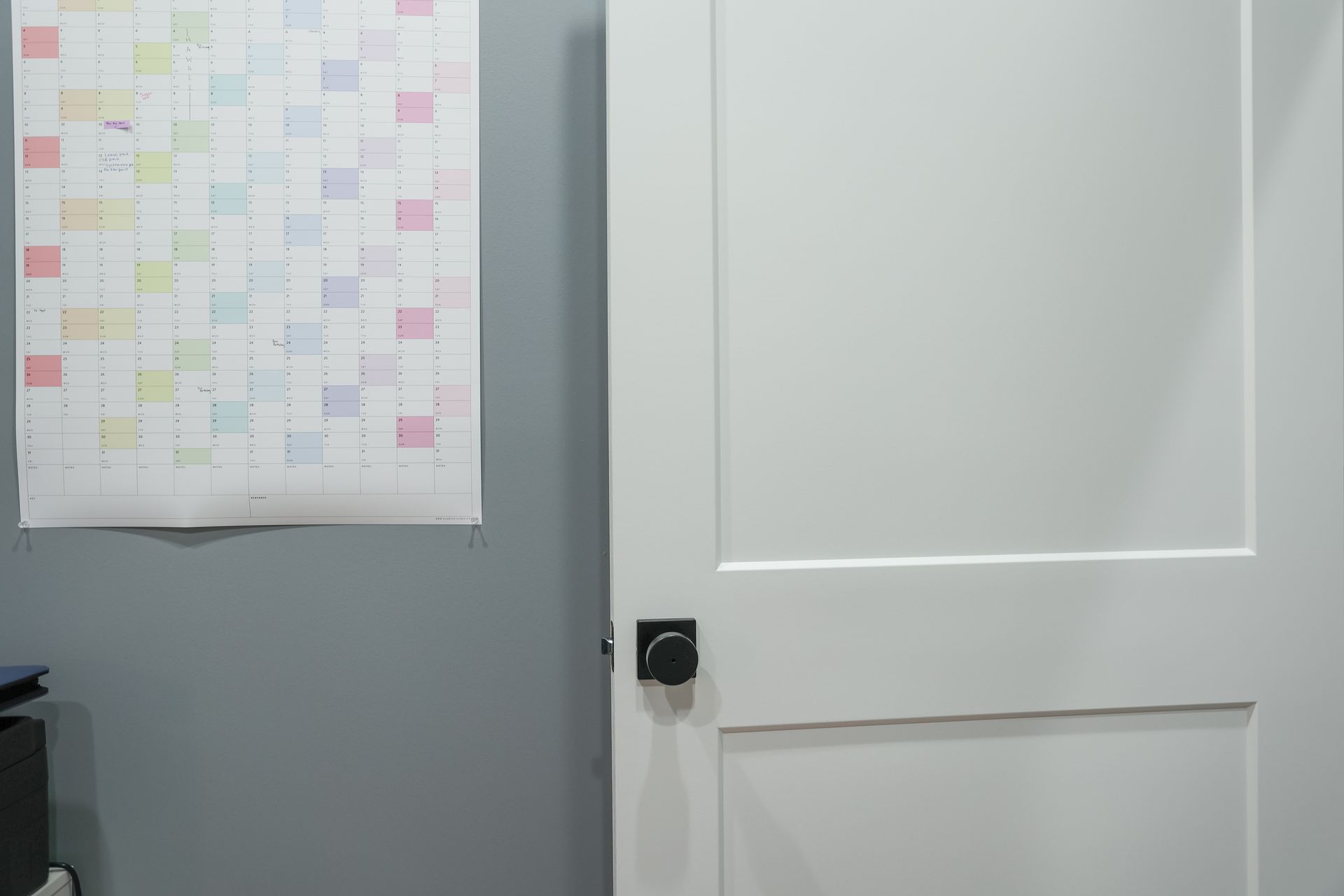 White door with black handle next to a calendar on a gray wall.