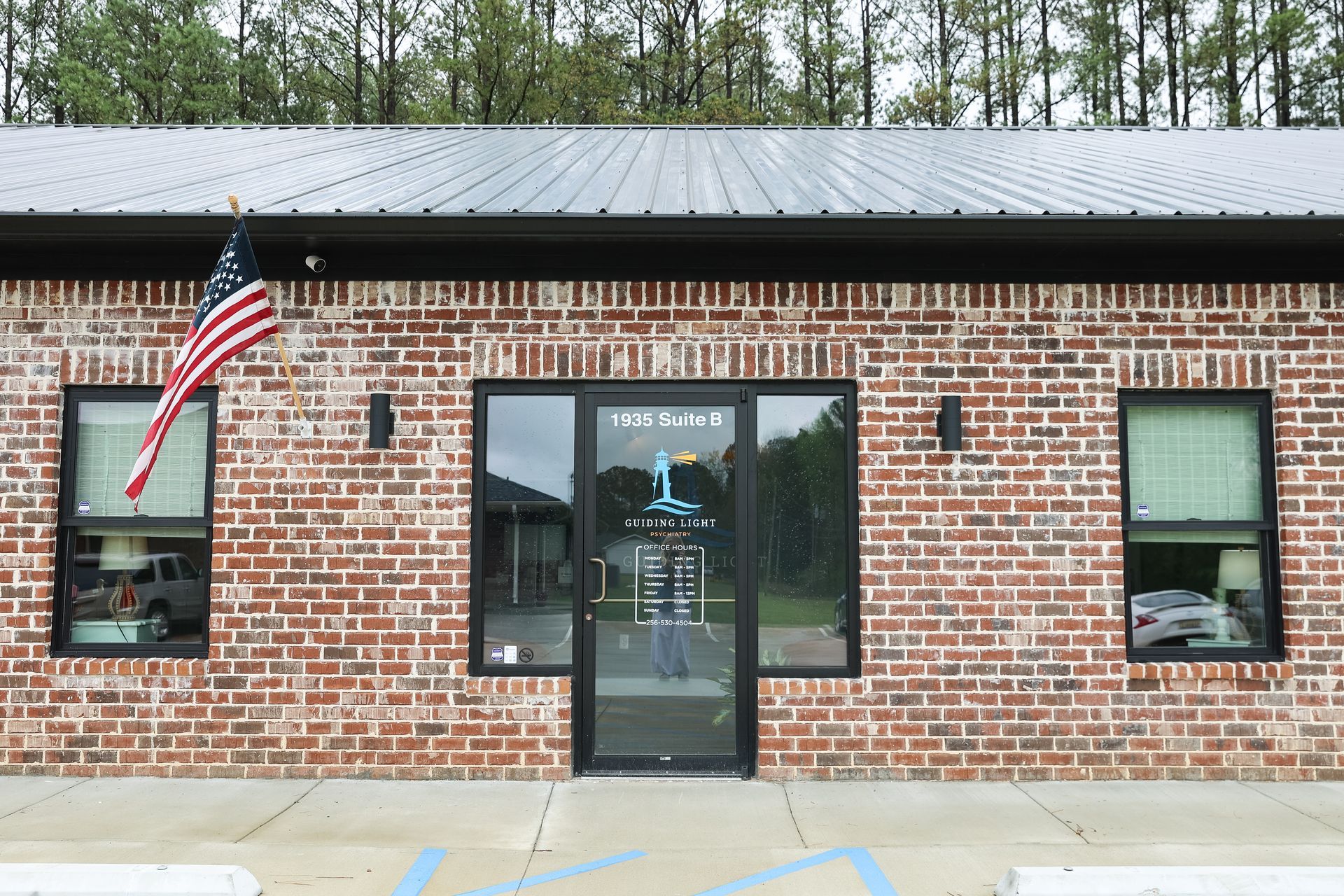 Brick building with glass door, windows, and American flag. 
