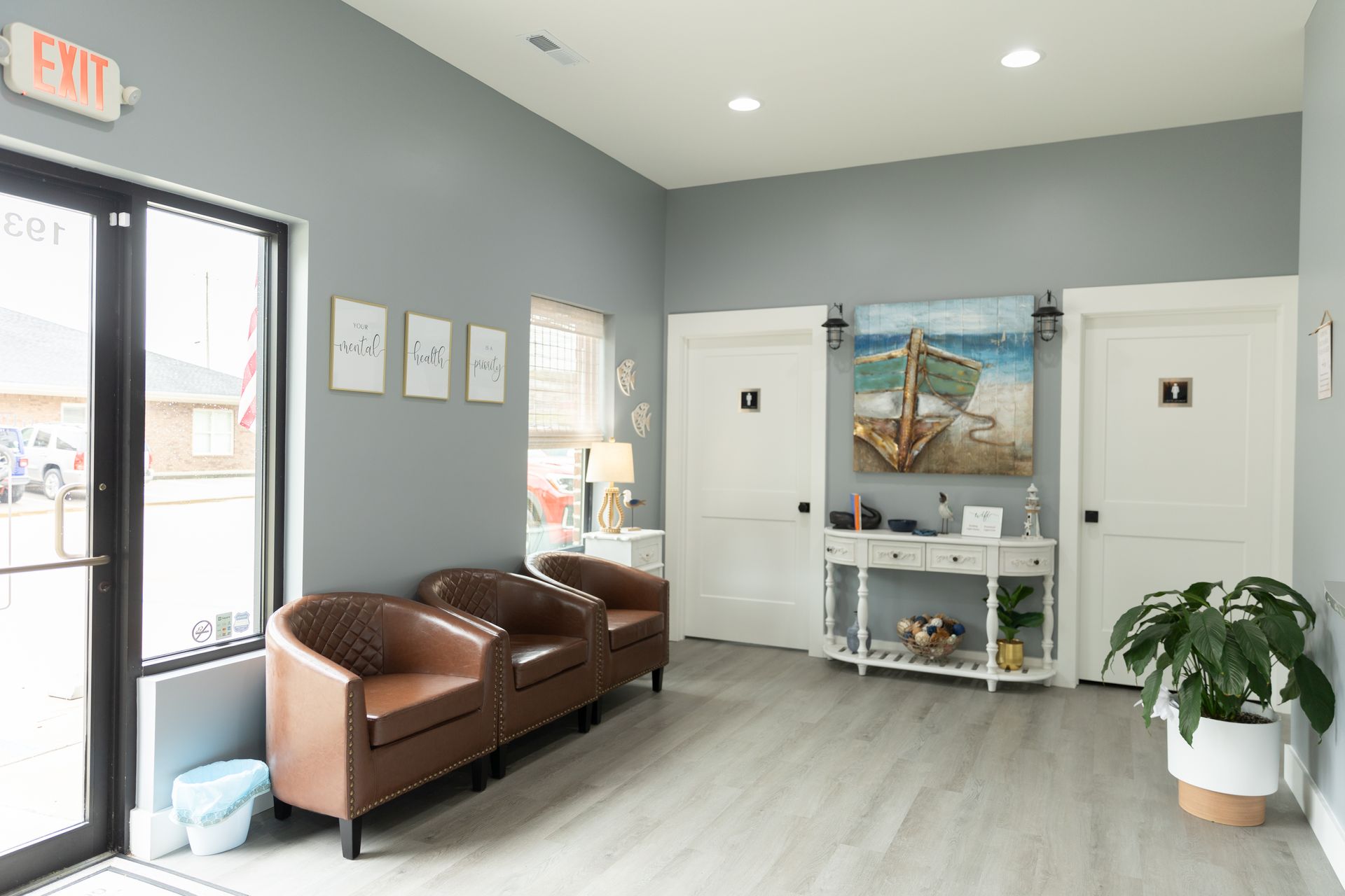 Interior view of a waiting room with brown chairs, light gray walls, art, and two white doors.