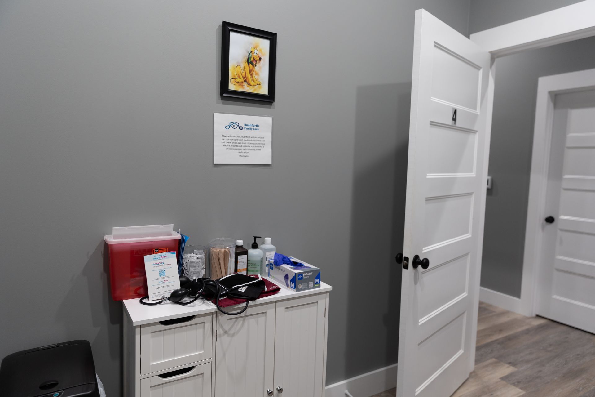A medical exam room with a cabinet of medical supplies and a partially opened door.