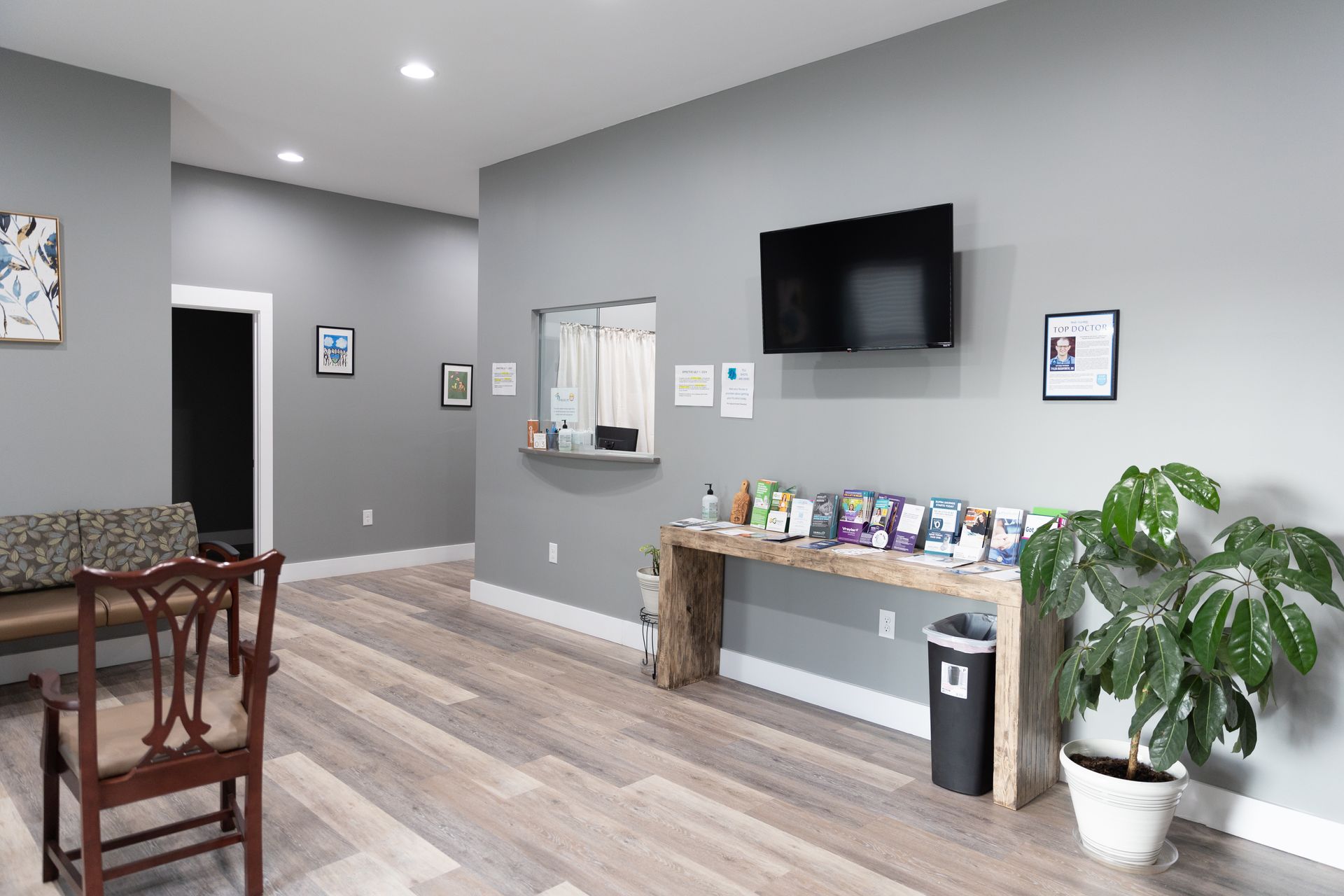 A vet clinic waiting area with a reception window, TV, and a potted plant.