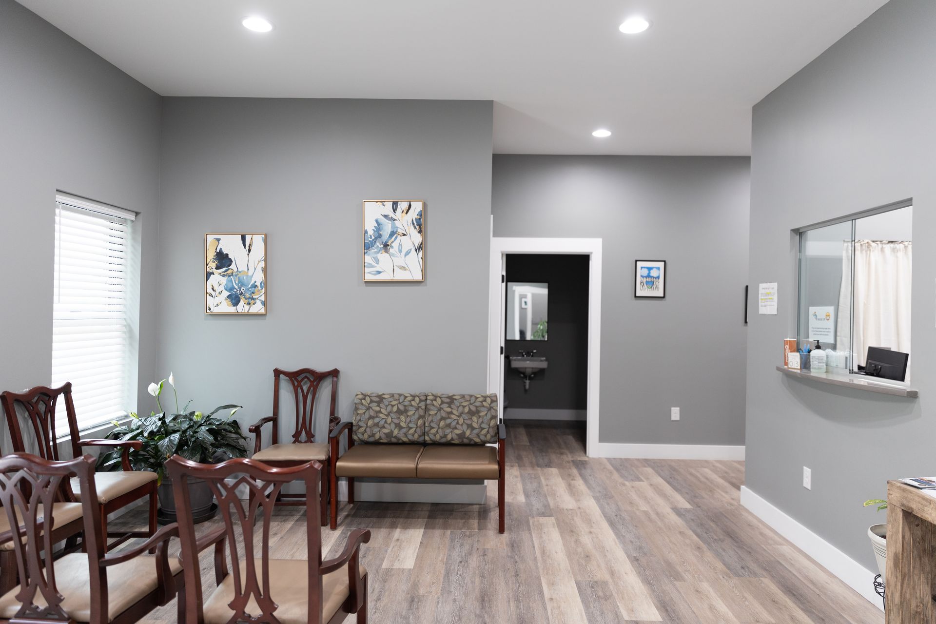 Waiting room with gray walls, wood-look floor, chairs, and two abstract paintings.