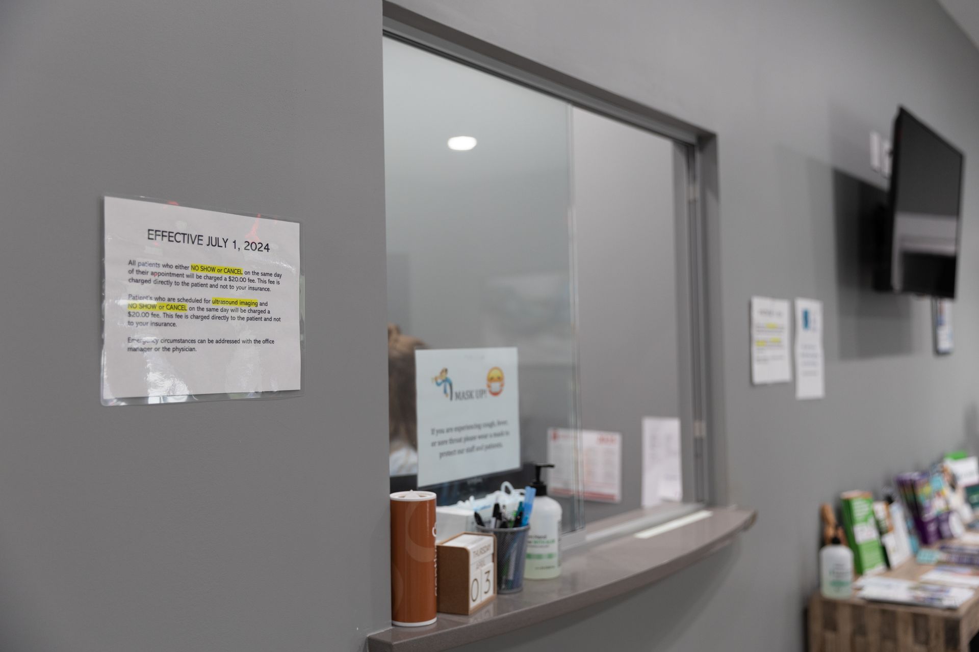 Gray office interior with a sign on the wall, a window, and a TV; a counter with items.