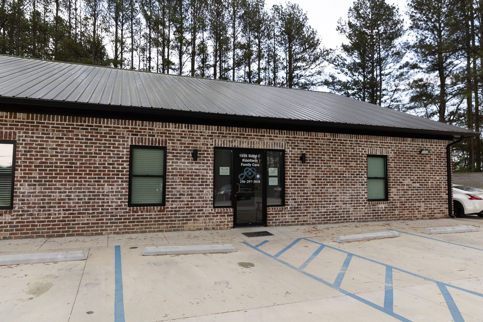 Brick building with metal roof; storefront with windows and parking spaces.