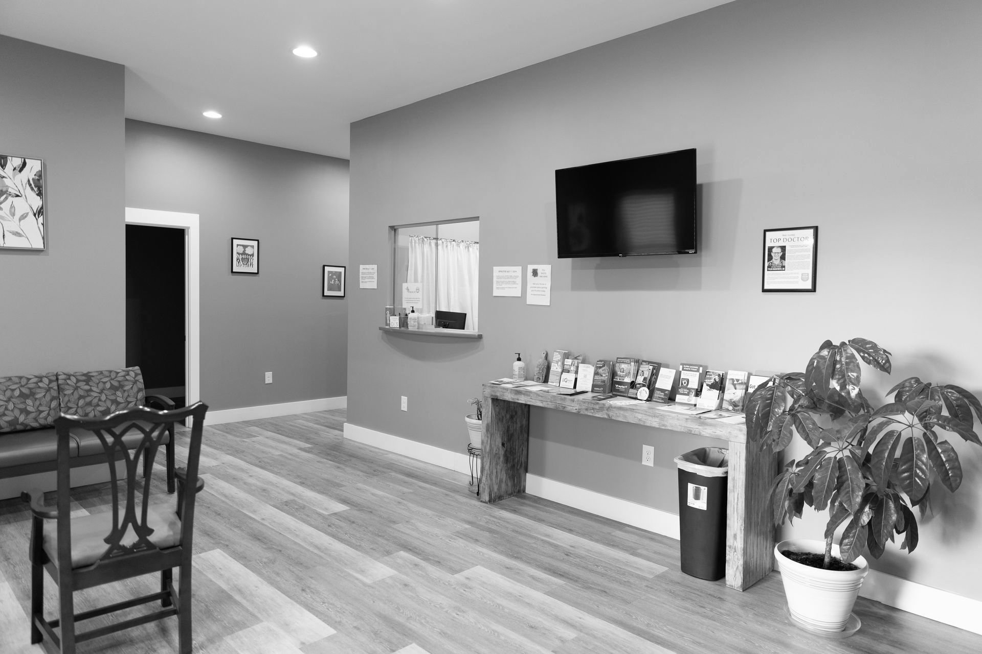 Waiting room with wood floors, reception window, TV, and potted plant.