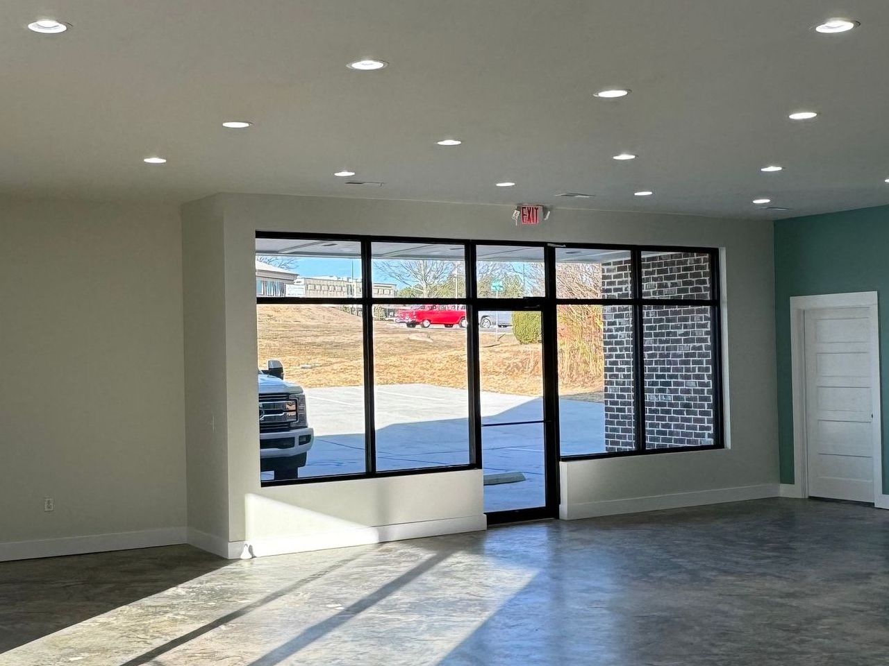 Interior of an empty commercial space with large windows, neutral walls, and a concrete floor.